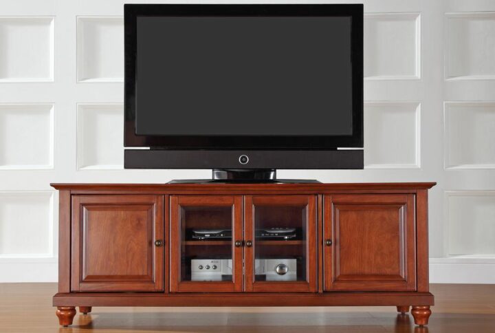 Enhance your living space with the impeccably-crafted Cambridge 60” Low Profile TV Stand. This beautiful TV stand accommodates most 65" flat-panel TVs and blends with a variety of home decor. Two cabinets have raised panel doors for concealed storage. The center cabinet has beveled glass doors that protect valued electronic components while allowing for complete use of remote controls. Adjustable shelving offers an abundance of versatility