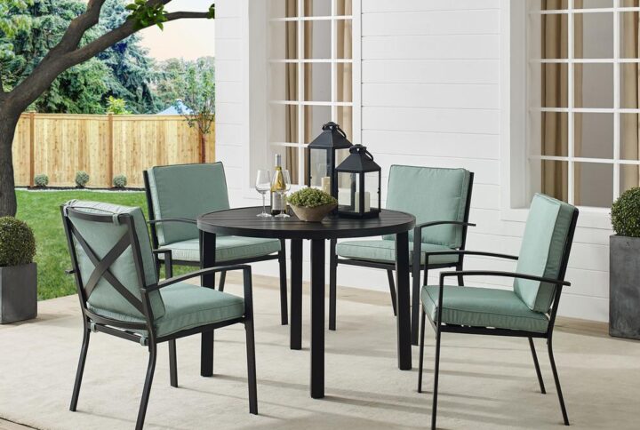 Gather around the Kaplan 5pc Round Dining Set for a cozy meal al fresco. The round table features a slatted design that elevates the sturdy steel construction creating a perfect partner to the four outdoor dining chairs. Each chair showcases comfy back and seat cushions plus a classic x-back design. The table has a standard umbrella hole that will allow you to add some shade on a hot summer day. Simple and stunning