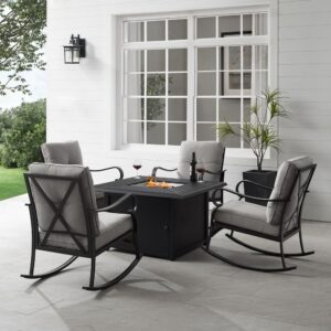 the rocking chairs offer cushioned seating perched atop smooth metal rockers. The chairs surround a propane-powered fire table with a slatted top and solid paneled base. With gas controls and a rack for a propane tank located inside the table's base