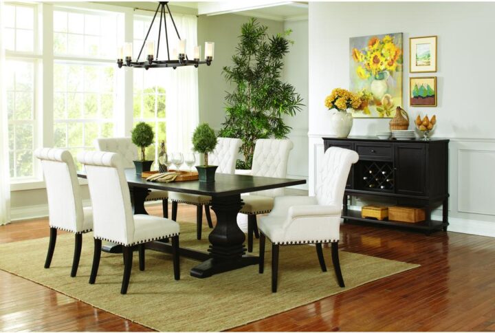 This spectacular 7-piece dining room set is a magnificent addition to the home. Rectangular dining table is meticulously crafted from wood with crisp straight lines. It sits on two broad legs fashioned with curved lines and defined angles with a trestle-like base. The four side chairs have luxurious cushions and rolled seatbacks with button tufting while the two armchairs also have stylish rolled armrests. Chairs are wrapped in stunning white fabric that goes well with contrasting dark nailhead trim and leg finish.