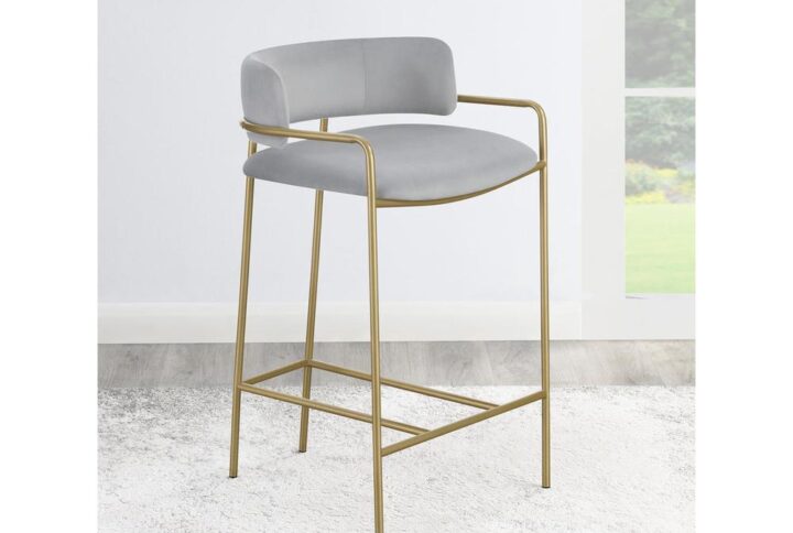 A soft and supple grey velvet envelops the comfy padded seat and linear backrest of this chic and glamorous stool. Situated and supported by a slim rod-like frame in a gold finish