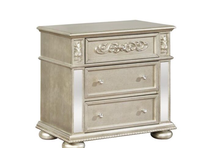 Keep necessities close at hand with this three drawer nightstand from the Heidi collection. The metallic platinum finish gives a glamorous look with mirrored accents. Three drawers offer ample space to organize those needed items. Ornate wood carved design offers additional intricate detail in this luxe nightstand. Pair two on either side of the bed for a symmetrical decor theme