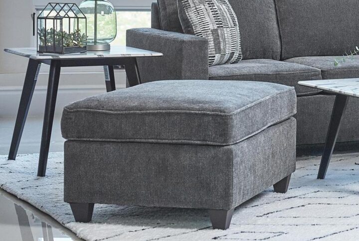 Prop your feet up or enjoy a temporary seat with this reversible transitional ottoman. But be aware - you may have competition from the family dog or cat for this comfortable accent piece. The plush dark grey chenille fabric cushion is accented with self-welt details for extra style. The dark brown tall tapered legs give the ottoman added height. It's ideal for use with your favorite sectional