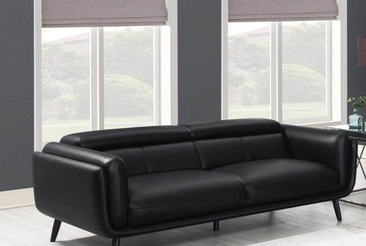 Make the most of tight living rooms with this sleek tuxedo-inspired contemporary sofa. Padded double track shelter arms embrace you as you kick back and unwind along the plush attached seat cushions and tall back. Slender flared legs present a retro throwback as a smooth black leatherette modernizes the mid-century modern frame design. Contrast cross-stitching and topstitching offer a finishing touch. A magnificent masculine-leaning sofa for modern homes.