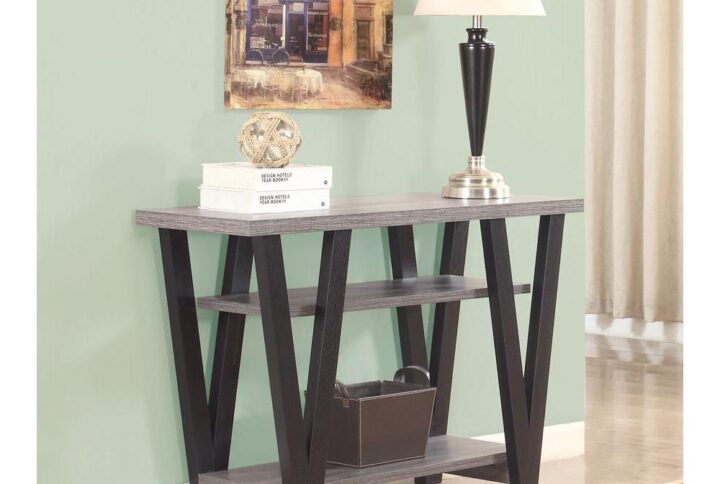 This impressive sofa table is crafted with mid-century modern sensibility that you'll appreciate. The big grey rectangular table top easily fits a table lamp and a volume of books. Two shelves below provide extra storage for a laptop and modem or simply decorative accessories. The four legs are finished in black with a V-shaped design that lends an extra vibrancy. Its prominent design and contrasting color pattern give it the versatility to match any decor.