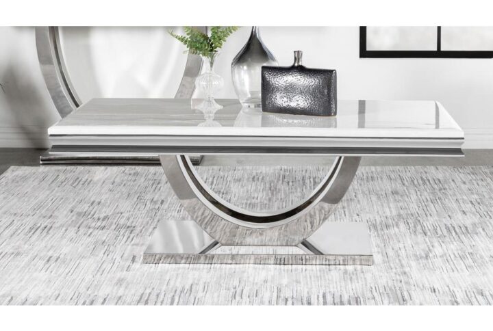 Transform your contemporary living room seating area with this modern glam coffee table. A large rectangle shaped top made of white engineered stone lends a timeless aesthetic with its marble-like resemblance. Two slender curved bars create a demilune shaped pedestal base that grounds the table and offers a sleek ultra-modern look and feel. Across the base is a gleaming polished chrome finish