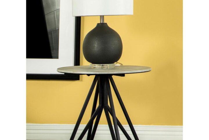 Industrial elements and sleek modern lines bring forth this modern end table. A metal butterfly-like base design of open and flared hairpin style legs in a gunmetal finish offer a striking visual interest to the furniture piece and the room in which is rests. Placed on top of the chic base is a round tabletop that portrays a molded cement for a rustic modern farmhouse flair. The cement-inspired top also offers a textured sandy feel to resemble the true material. Place this modern end table beside an accent chair or allow it to showcase a sculpture or art piece in a loft studio.