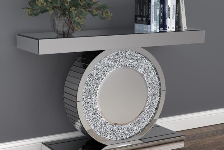 Glam up your living space with this contemporary console table. This silver finish console table has a mirrored effect for a punch of contemporary glam. The geometric design displays a disc body framed by a rectangular base and tabletop for a sculptural aesthetic. Silver accent crystals provide textural dimension to the circular body. This contemporary console table works well in a space with a Hollywood glam theme.