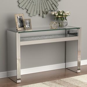 Keep a crisp linear décor theme with this console table. The clean lines form two square leg bases bridged by a shallow shelf with floating glass top above. The silver finish adds to the glamorous look of this striking piece. This silver console table adds a dramatic sculptural element to a living room or entertaining space. Top with a sculptural art piece for a truly captivating focal point.