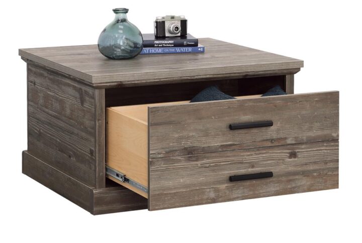 The cool and neutral Pebble Pine finish of this storage coffee table from the Aspen Post collection will bring the feel of a rustic