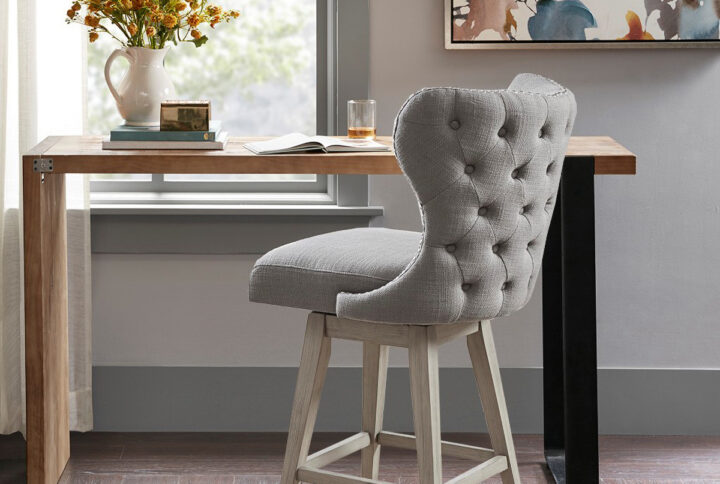 The Madison Park Hancock Swivel High Wingback Button Tufted Upholstered Counter Stool with Nailhead Accent complements any decor with its simple