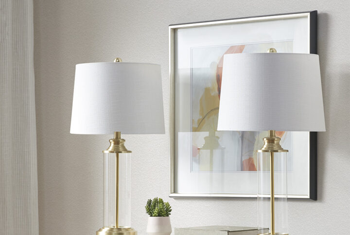 Update your living room or bedroom with the sleek style of the Clarity Glass Cylinder Table Lamp set of 2. The base is made from metal and glass with a gold finish