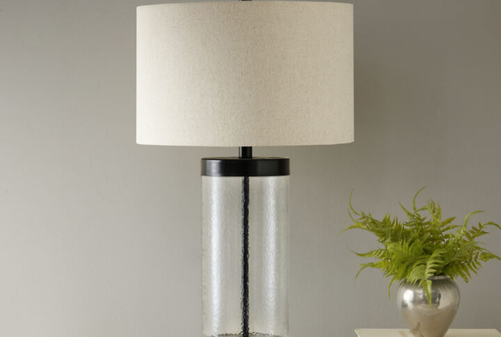 Add an elegant charm to your home with the INK+IVY Macon Glass Cylinder Table Lamp. This stylish table lamp is made from a painted bronze metal and a clear glass base that adds dimension and charm. A drum shade shape helps accentuate the design. Illuminate your living room or bedroom with this gorgeous table lamp. One Type A light bulb is needed and included.