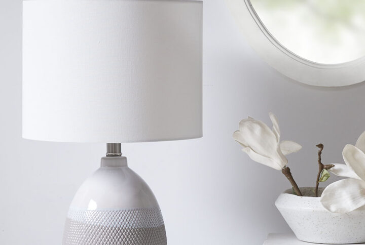 Update your space with the sleek style of the Driggs Ceramic Textured Table Lamp. The base is made from ceramic with a painted Ivory/Grey and white finish for a sleek gradient look. The drum shaped white shade softly filters the light