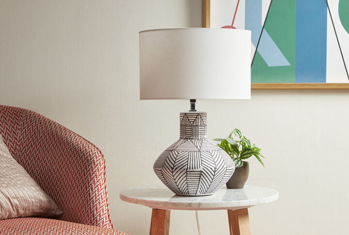 Make a statement with the modern style of the INK+IVY Agape Boho Ceramic Table Lamp. This round table lamp features a gourd-inspired base flaunts a geometric stripe pattern against the white finish to create a bold contrasting design. A round drum lamp shade acts as a soft light filter to create a warm ambiance