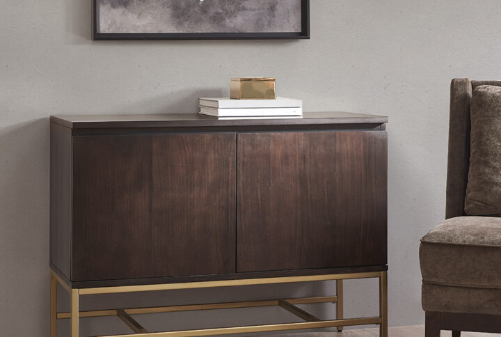 The Martha Stewart Allister Accent Cabinet offers a sleek modern storage update to your home. This accent chest features a brown wood finish on the solid wood frame with a gold metal base