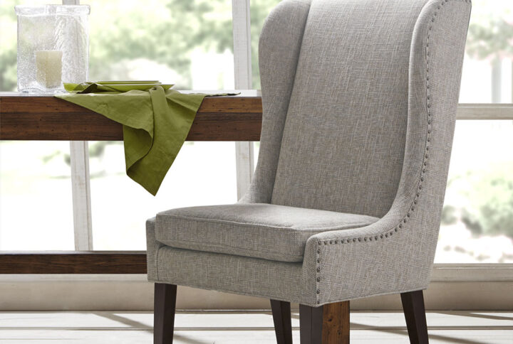 Complete your dining room decor with the Madison Park Garbo Captains Dining Chair. This chair features a high wing back design that will leave a monument impression for your guests.  Upholstered in a heather grey fabric and elevated with bronze nail head accents. The frame is supported on solid wood legs in a dark espresso wood finish.  Removable cushions